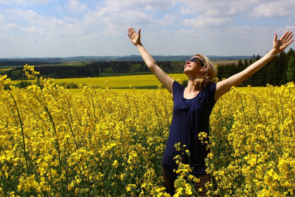 Mulher, com blusa de cor azul, em pé em meio a flores amarelas: mensagem de gratidão